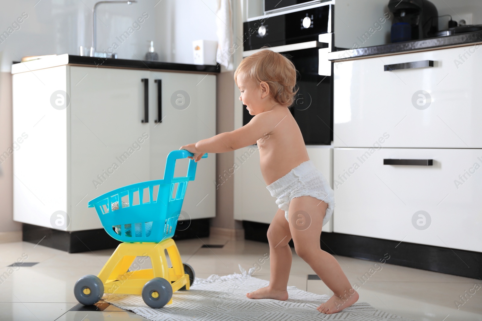 Photo of Cute baby with toy walker in kitchen. Learning to walk