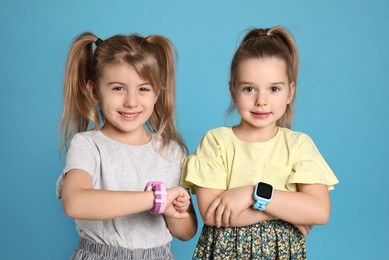 Little girls with smart watches on light blue background