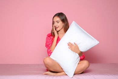 Beautiful teen girl hugging pillow on bed against color background