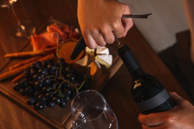 Photo of Romantic dinner. Man opening wine bottle with corkscrew at table indoors, above view