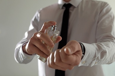 Photo of Man applying perfume on wrist against light background, closeup