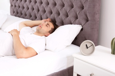 Young man sleeping in bed and alarm clock on nightstand at home