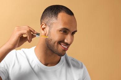 Handsome man applying cosmetic serum onto face on light brown background, space for text