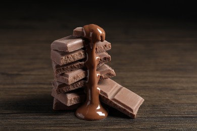 Photo of Pieces of milk chocolate with tasty paste on wooden table, closeup