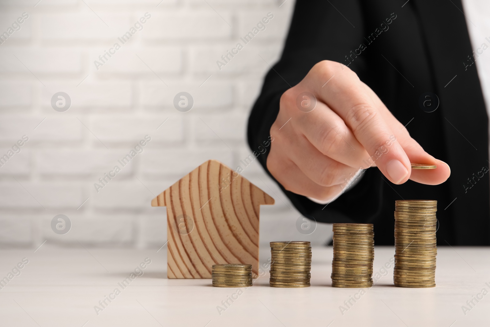 Photo of Woman stacking coins near wooden house model at light table, closeup. Space for text