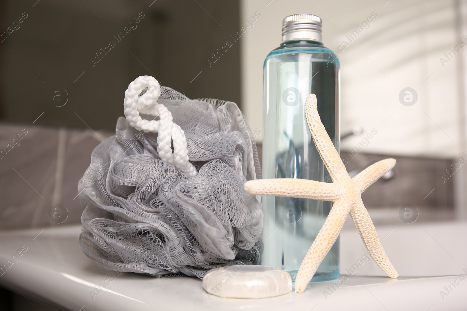 Photo of Grey sponge, starfish and shower gel bottle on washbasin in bathroom