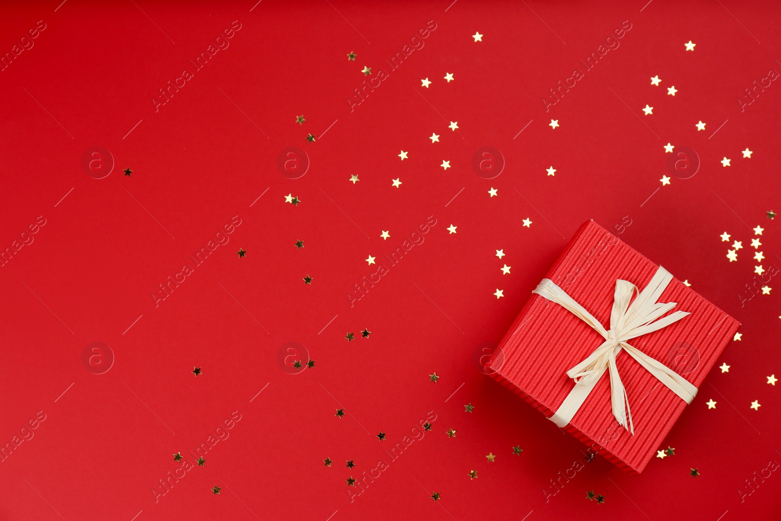 Photo of Gift box and shiny confetti on red background, top view. Space for text