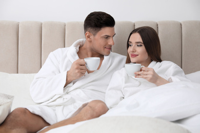 Photo of Happy couple in bathrobes with coffee on bed at home