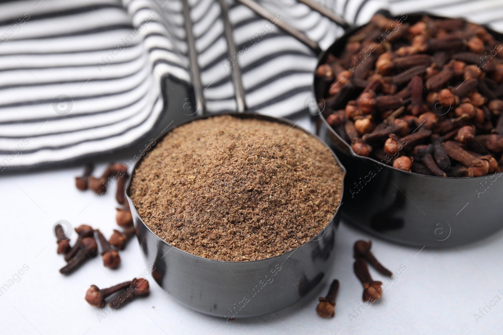 Photo of Aromatic clove powder and dried buds in scoops on white table, closeup