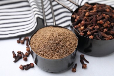 Aromatic clove powder and dried buds in scoops on white table, closeup