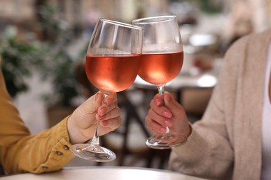 Photo of Women clinking glasses with rose wine at white table in outdoor cafe, closeup