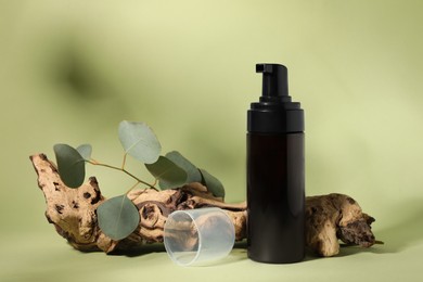 Bottle with face cleansing product, eucalyptus leaves and log on light green background