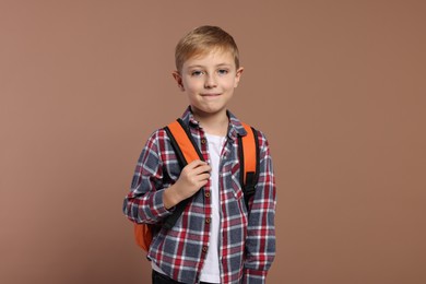 Happy schoolboy with backpack on brown background