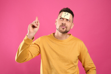 Emotional man with question mark on pink background