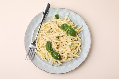 Photo of Plate of delicious trofie pasta with cheese, basil leaves and fork on beige background, top view