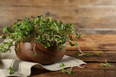 Photo of Fresh radish microgreens in bowl on wooden table, space for text