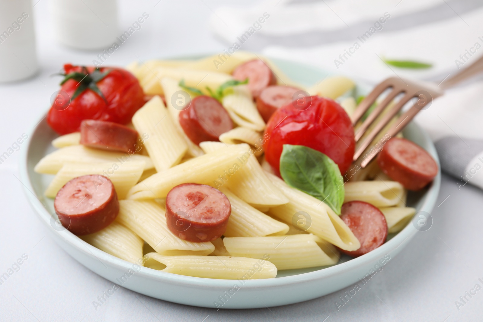 Photo of Tasty pasta with smoked sausage, tomatoes and basil on white table, closeup