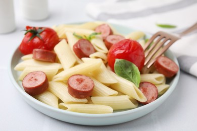 Tasty pasta with smoked sausage, tomatoes and basil on white table, closeup