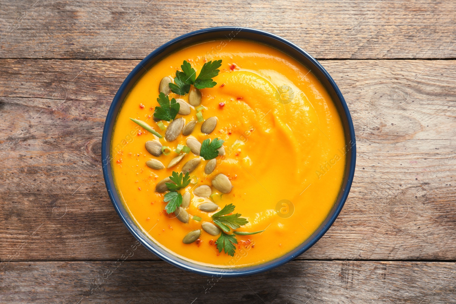 Photo of Delicious pumpkin cream soup in bowl on wooden background, top view