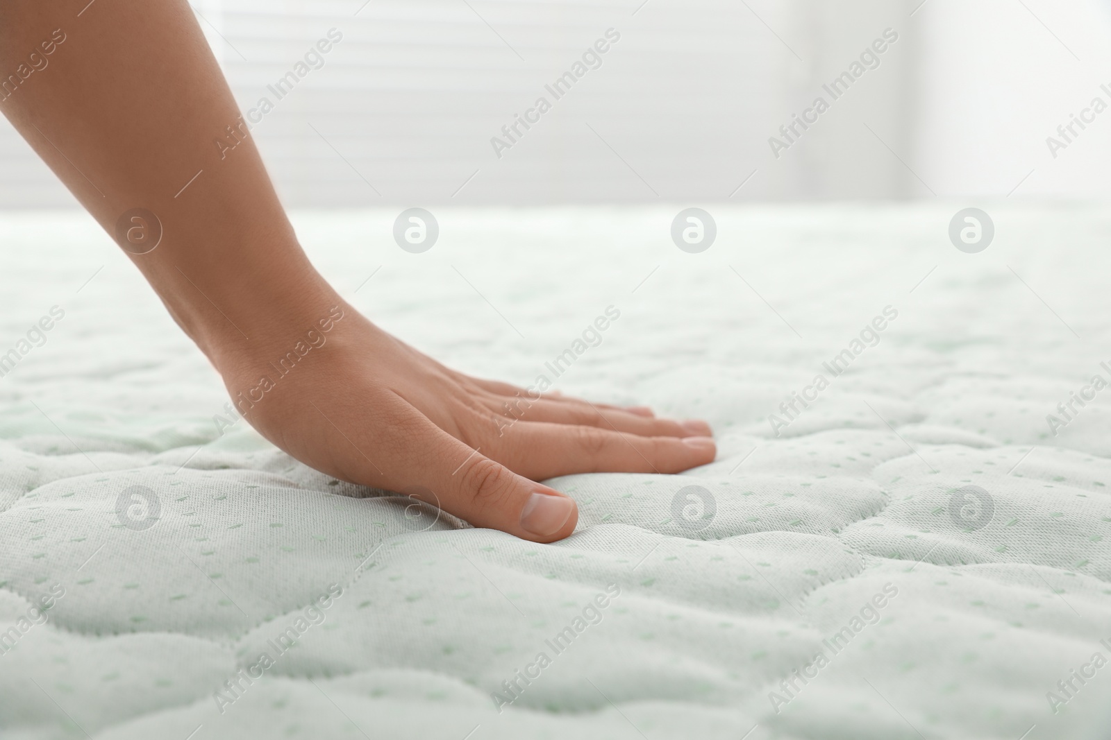 Photo of Woman touching soft light green mattress indoors, closeup