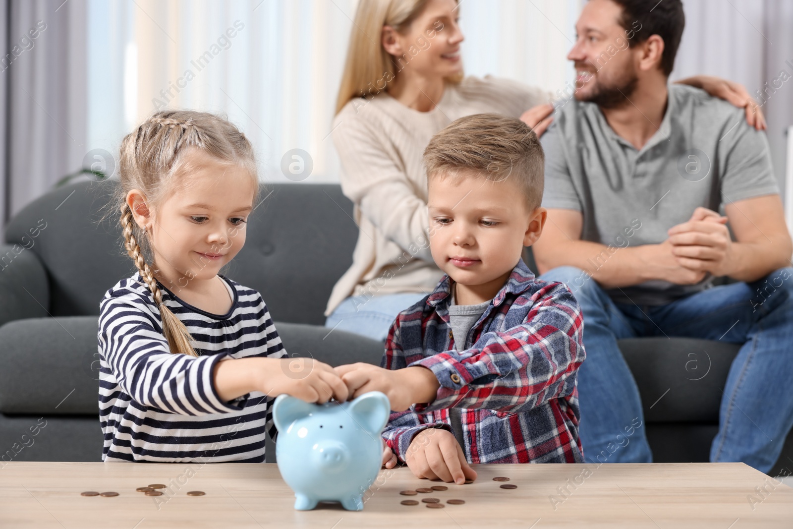 Photo of Family budget. Children putting coins into piggy bank and their parents at table indoors, selective focus