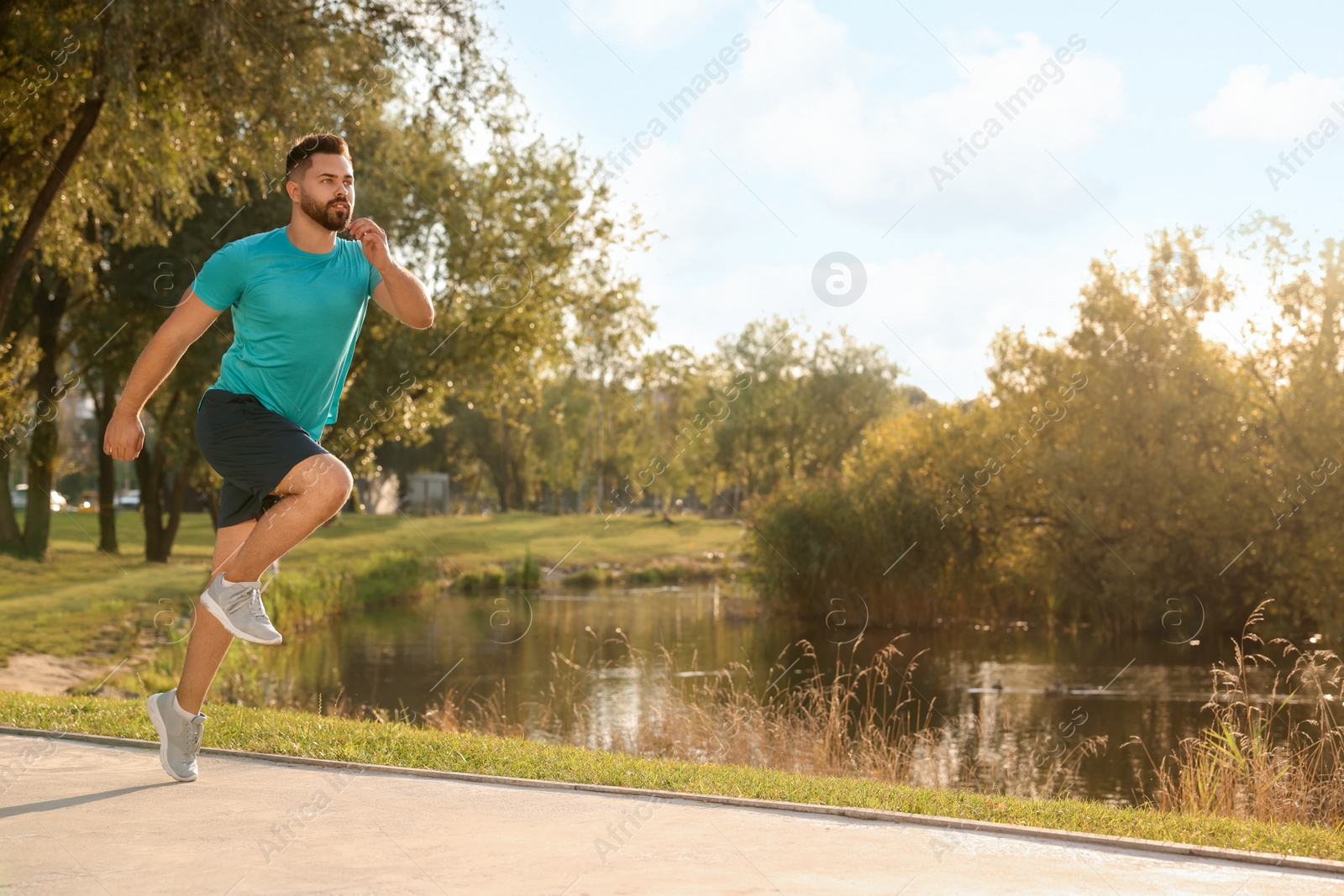 Photo of Young man running near pond in park. Space for text