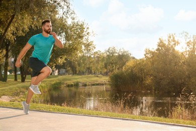 Young man running near pond in park. Space for text