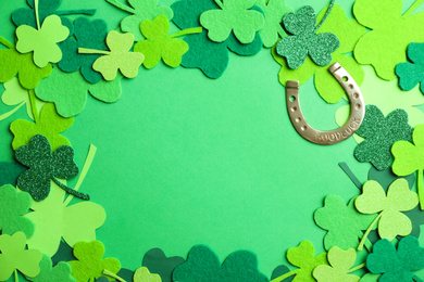 Photo of Frame made of clover leaves and horseshoe on green background, flat lay with space for text. St. Patrick's day