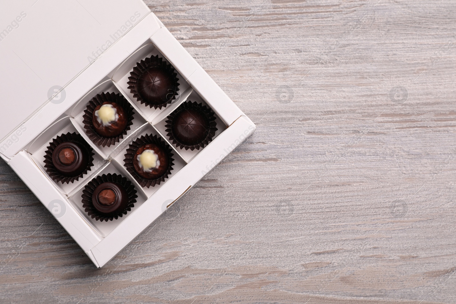 Photo of Delicious chocolate candies in box on white wooden table, top view and space for text. Production line