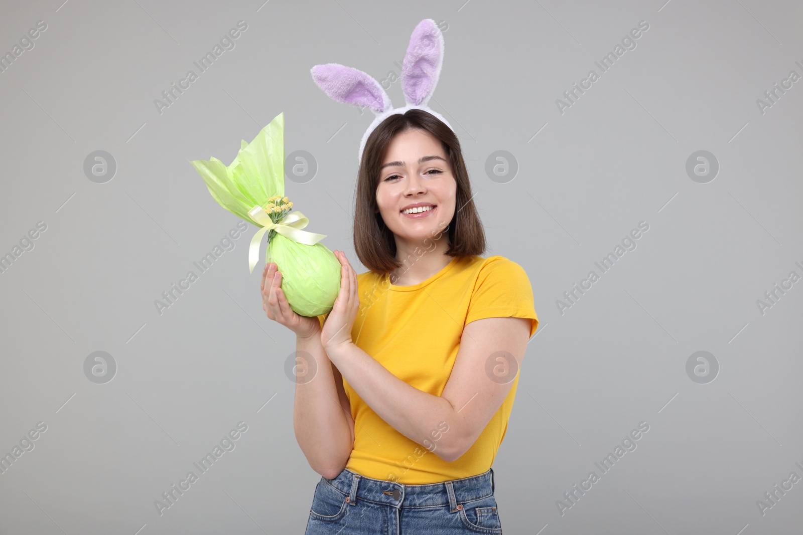 Photo of Easter celebration. Happy woman with bunny ears and wrapped egg on grey background