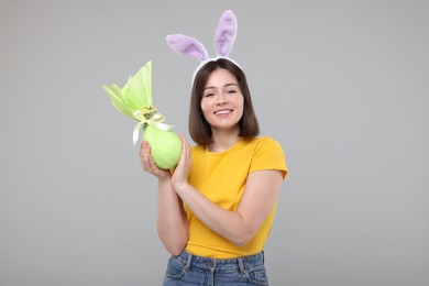 Easter celebration. Happy woman with bunny ears and wrapped egg on grey background