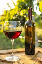 Photo of Bottle and glass of red wine on wooden table in vineyard