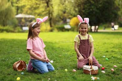 Photo of Easter celebration. Cute little girls in bunny ears hunting eggs outdoors