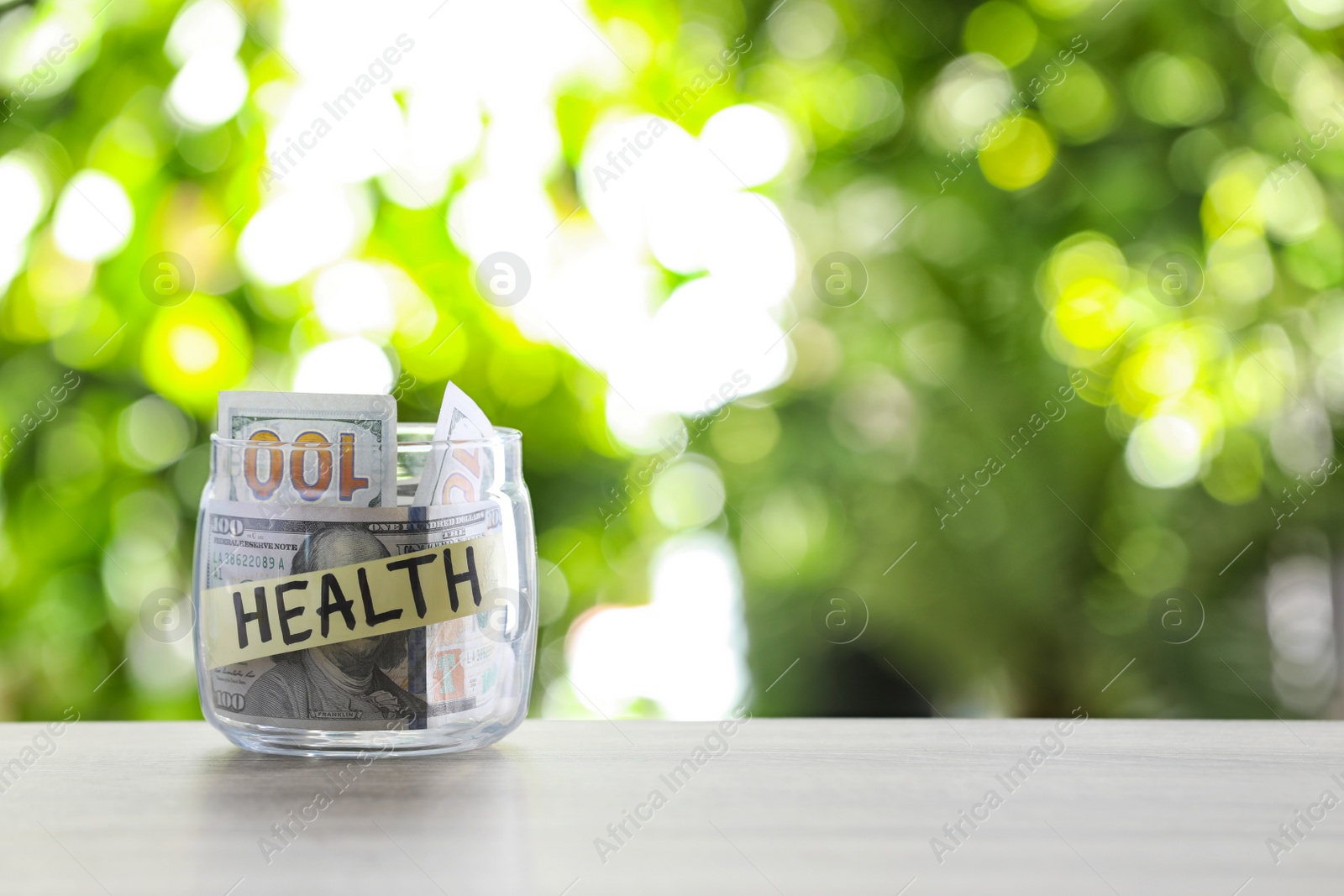 Photo of Glass jar with money and label HEALTH on table against blurred background. Space for text