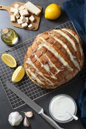 Freshly baked bread with tofu cheese, ingredients and knife on black table, flat lay