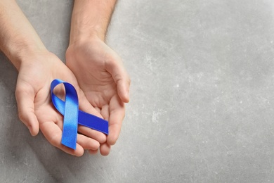 Photo of Man holding blue ribbon on grey background. Cancer awareness