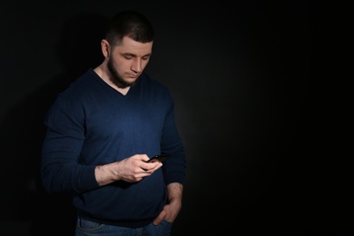 Photo of Young man engaged in smartphone on dark background, space for text. Loneliness concept