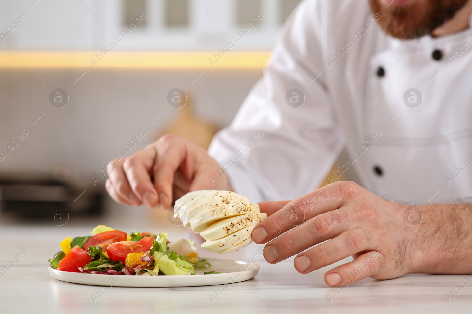 Photo of Closeup of professional chef adding mozzarella into delicious salad at marble table indoors, selective focus
