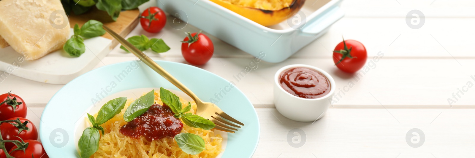 Image of Tasty spaghetti squash with tomato sauce, cheese and basil served on white wooden table. Banner design with space for text