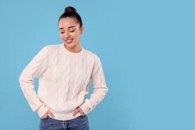 Photo of Beautiful young woman in stylish warm sweater on light blue background, space for text