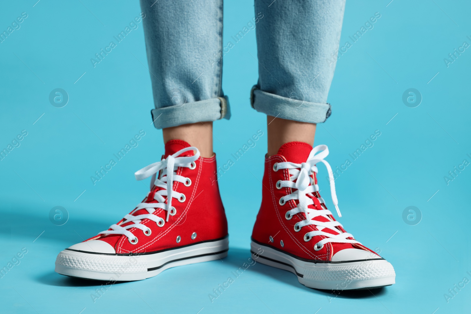 Photo of Woman in stylish gumshoes on light blue background, closeup