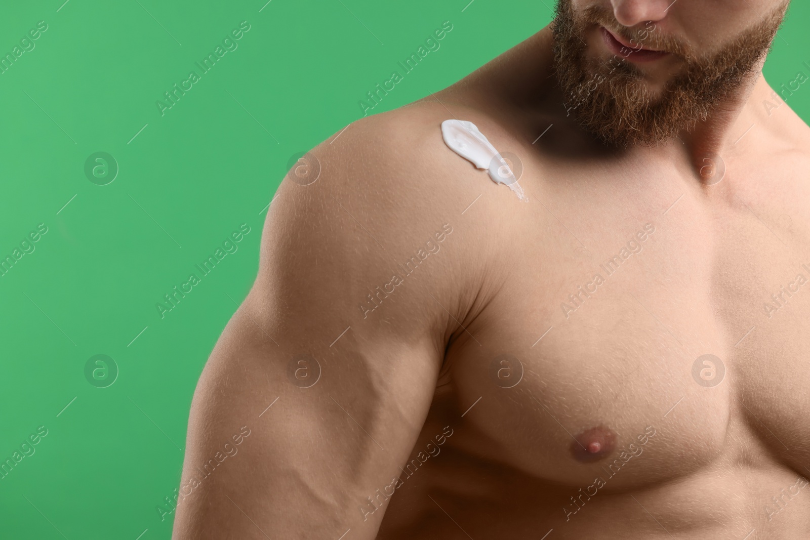 Photo of Man with moisturizing cream on his shoulder against green background, closeup