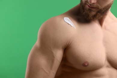 Photo of Man with moisturizing cream on his shoulder against green background, closeup