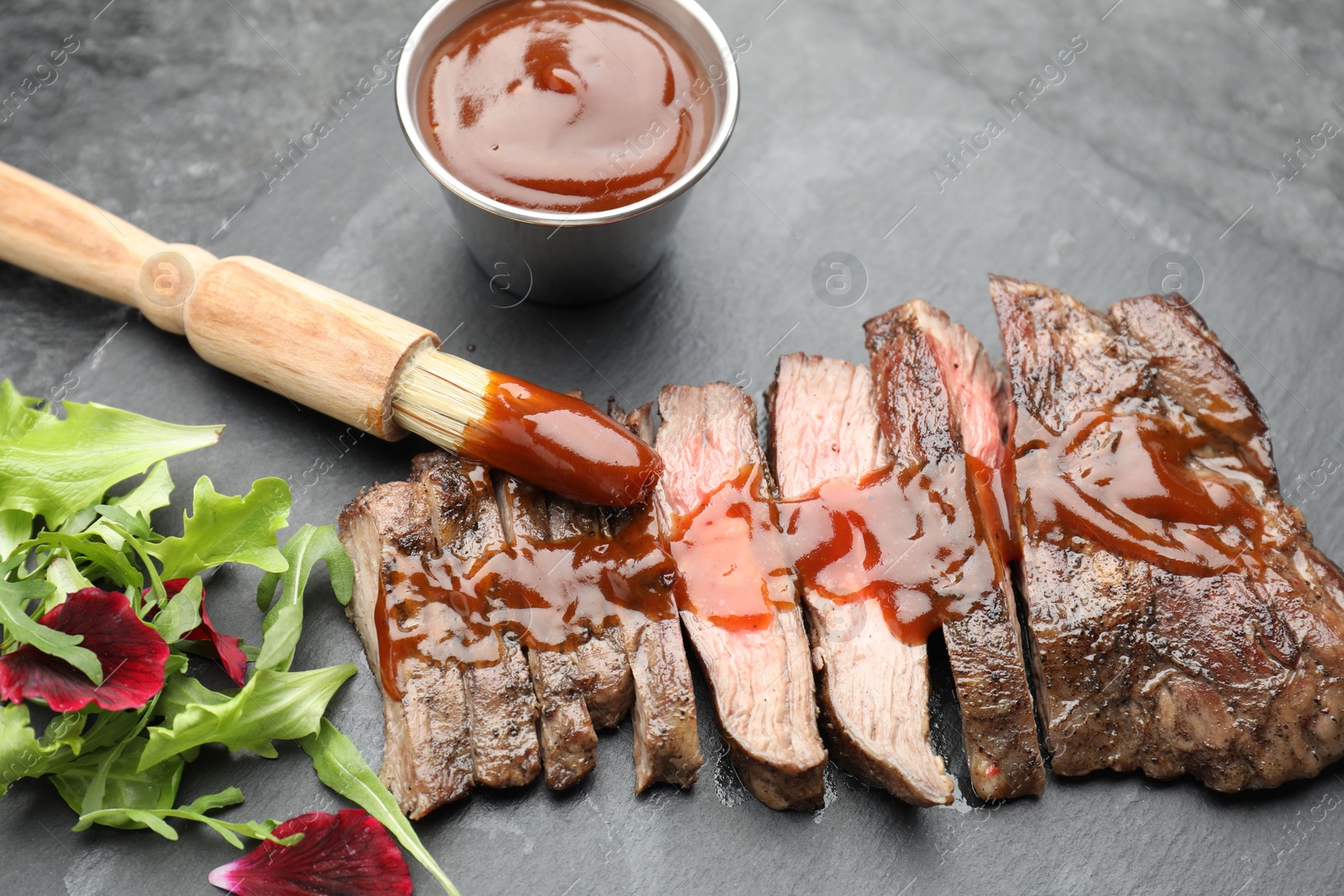 Photo of Pieces of delicious roasted beef meat with sauce and greens on black table, closeup