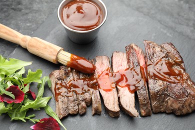 Photo of Pieces of delicious roasted beef meat with sauce and greens on black table, closeup