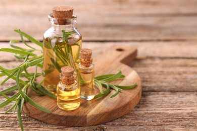 Aromatic essential oils in bottles and rosemary on wooden table, closeup. Space for text