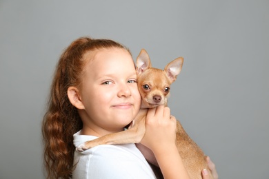 Photo of Little girl with her Chihuahua dog on grey background. Childhood pet