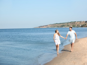 Happy young couple holding hands at beach on sunny day