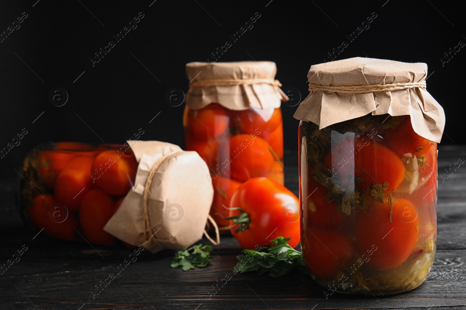 Photo of Pickled tomatoes in glass jars on black wooden table