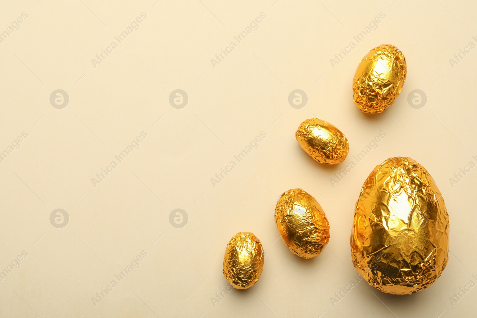 Photo of Chocolate eggs wrapped in golden foil on beige background, flat lay. Space for text